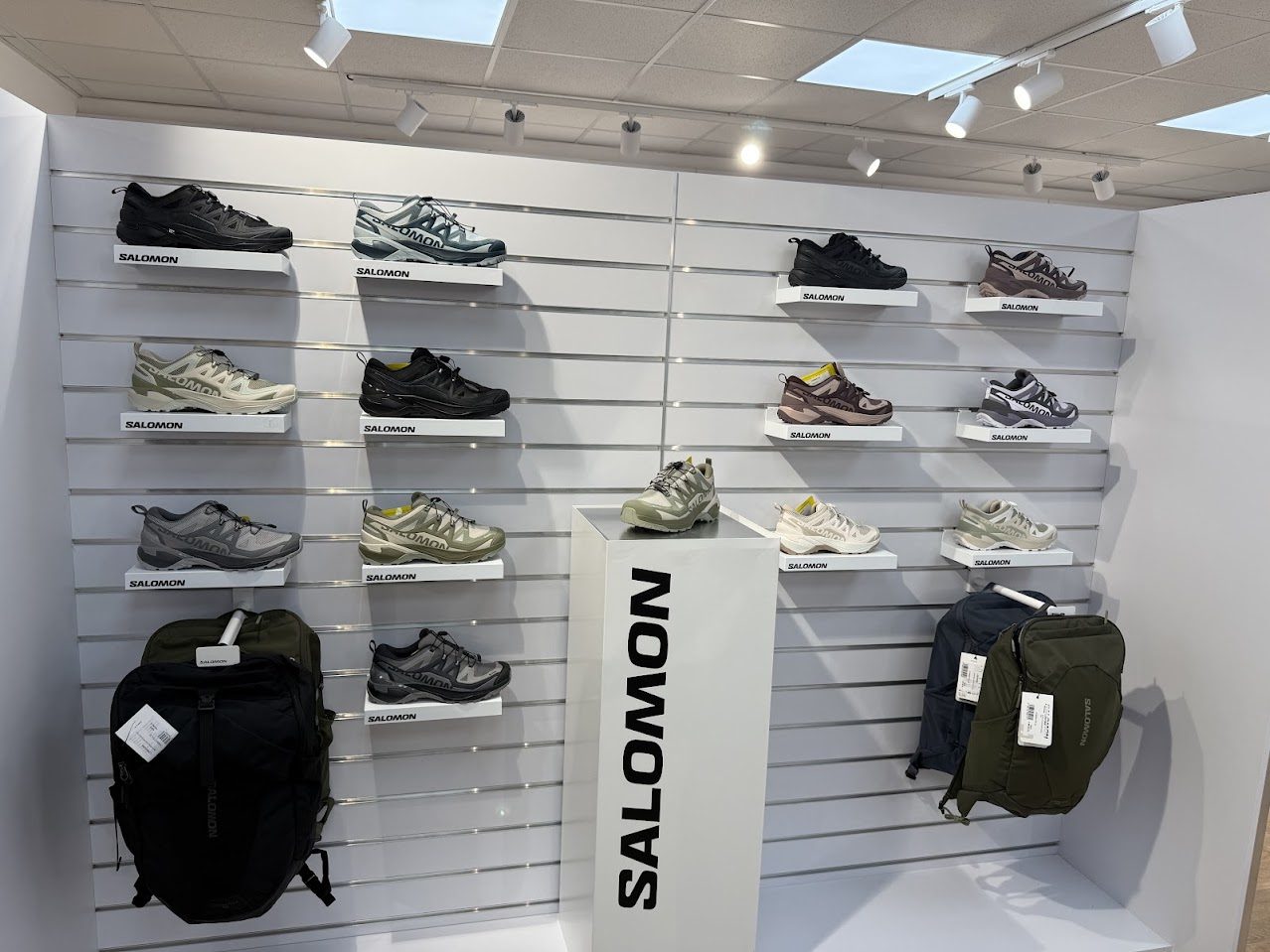 Un perete cu modele de pantofi sport și rucsacuri Salomon